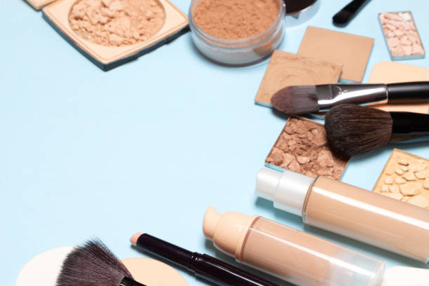 A collection of various makeup products including primers, powders, and brushes on a light blue background.