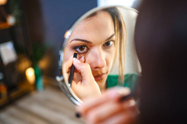 Woman applying kajal makeup to her eyes using a mirror for a bold and beautiful look.