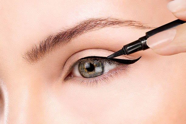 Close-up of a hand applying dramatic black eyeliner on an eyelid, illustrating eyeliner styles.