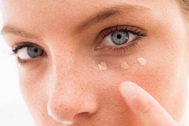 Close-up of a person applying dots of concealer under their eye, demonstrating proper concealer application.